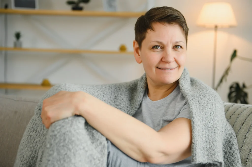 Middle-aged woman sitting on a couch wrapped in a grey blanket, smiling at home after receiving tenant support in Galway.