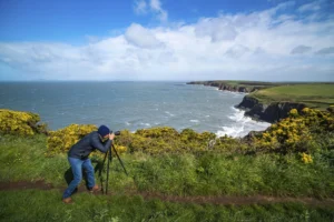 Photographer taking pictures of Irish cliffs and sea — representing grassroots fieldwork and local impact.